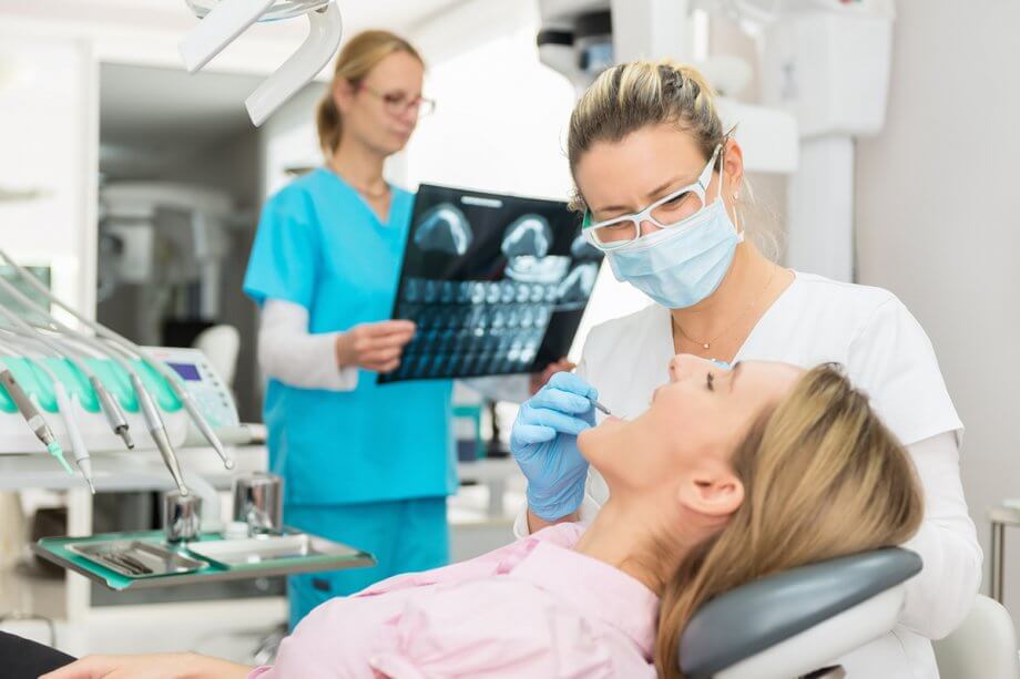 dentist examining female patient while dental hygienist reviews x-rays